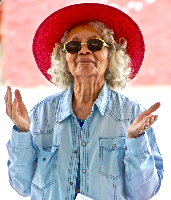 Joyful senior woman wearing a vibrant red hat and sunglasses, expressing happiness outdoors.